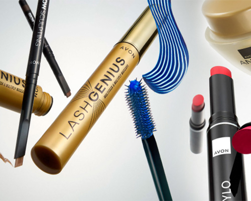 Koláž dekorativní kosmetiky Avon včetně řasenky Lash Genius ve zlatém obalu, modrého kartáčku, rtěnky a tužky na obočí.