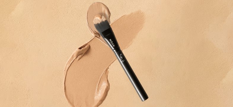 Černý štětec na make-up na béžovém pozadí s rozmazaným make-upem.
